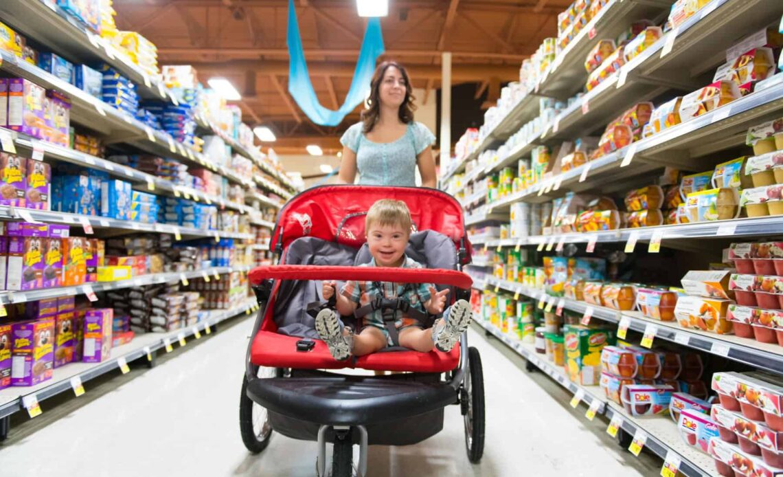 A woman shops in a grocery store while pushing a stroller with a child