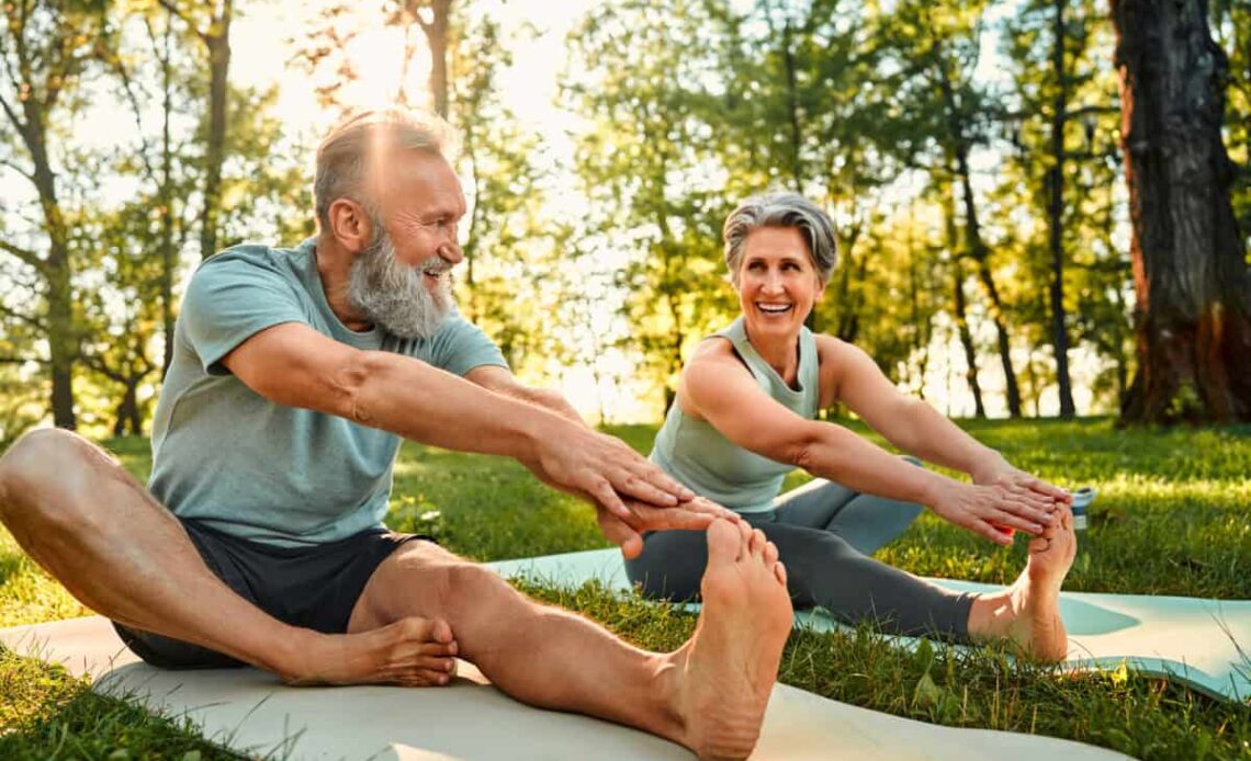 senior man and woman stretch their legs on yoga mats outside
