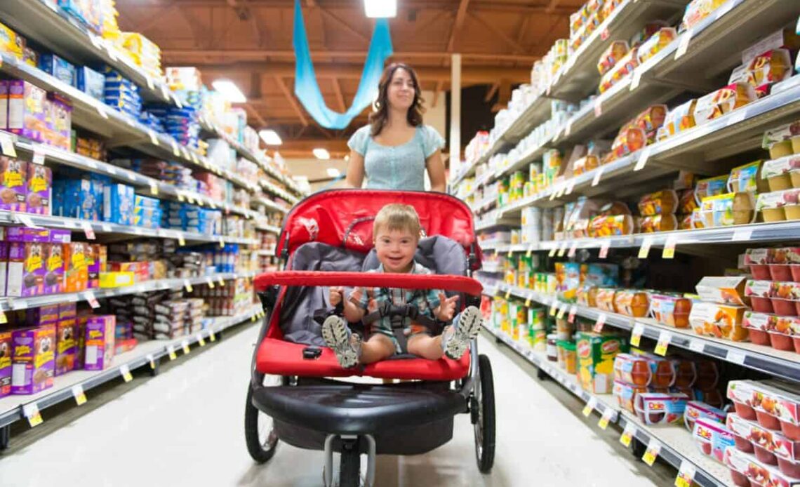 A woman shops in a grocery store while pushing a stroller with a child